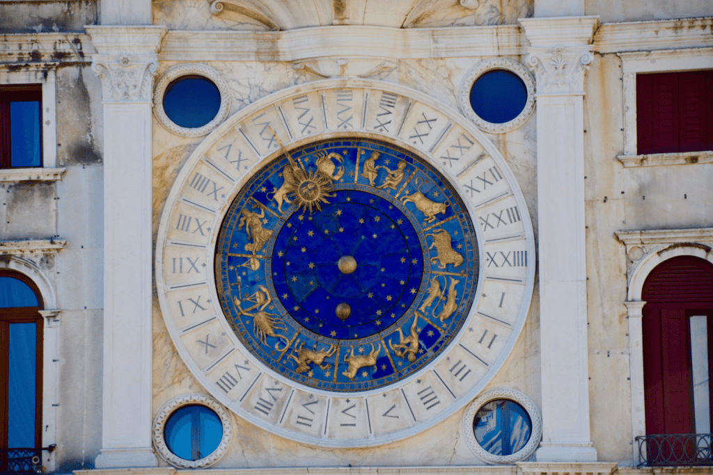 Photo blue and gold zodiac clock with astrological symbols displayed on a historic building facade.
